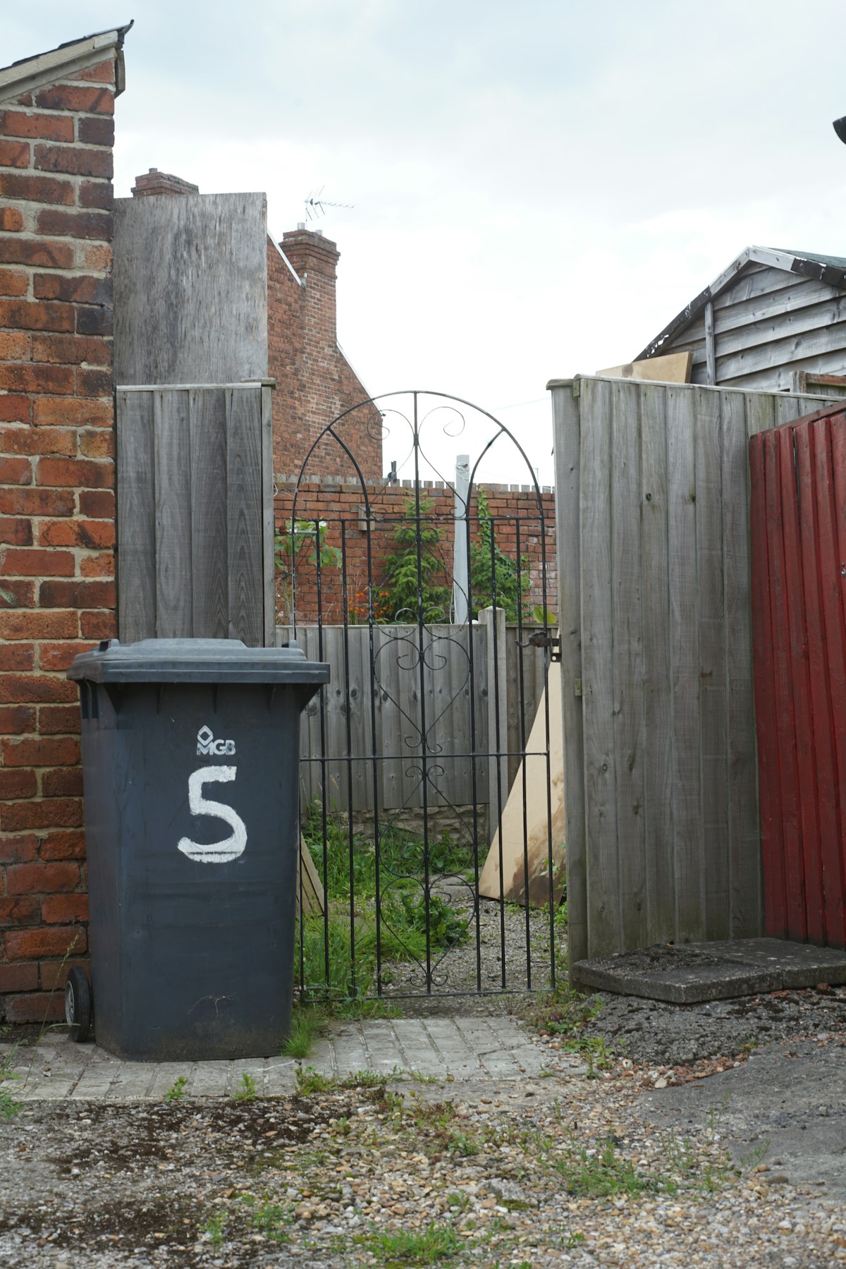 A wheelie bin by a garden fence